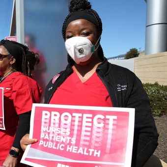 Nurs holds sign "Protect Nurses, Patients, Public Health"